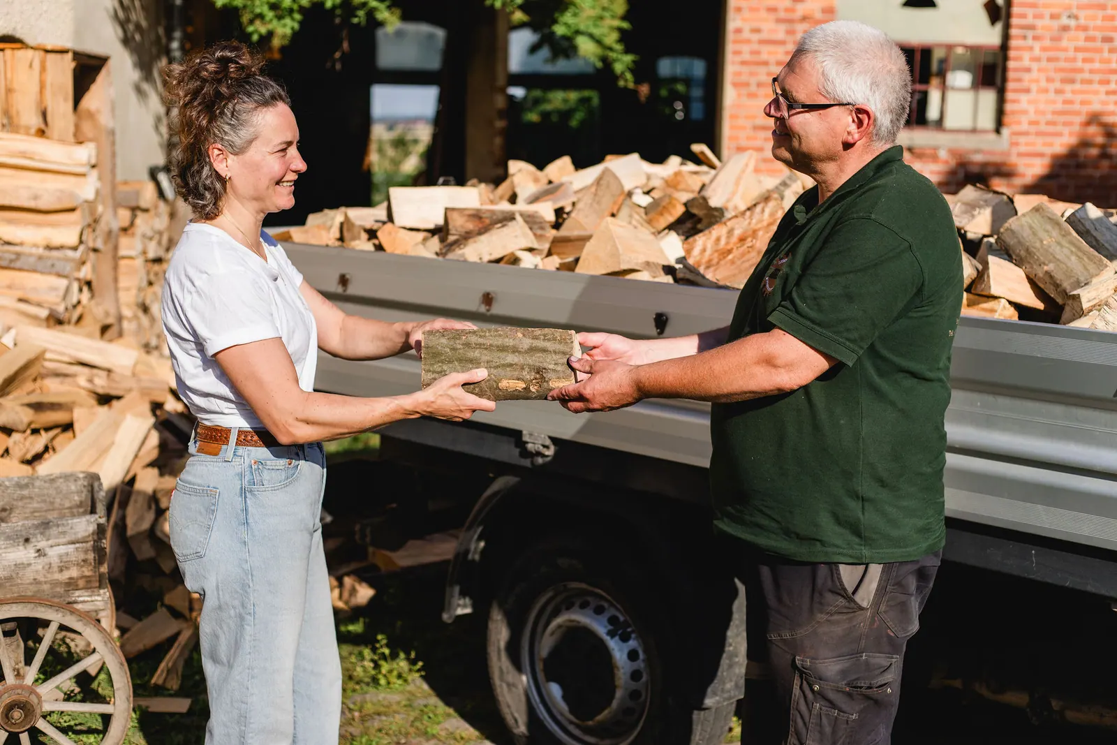 Karsten Garbe und eine Frau halten gemeinsam einen Holzscheit am Transporter